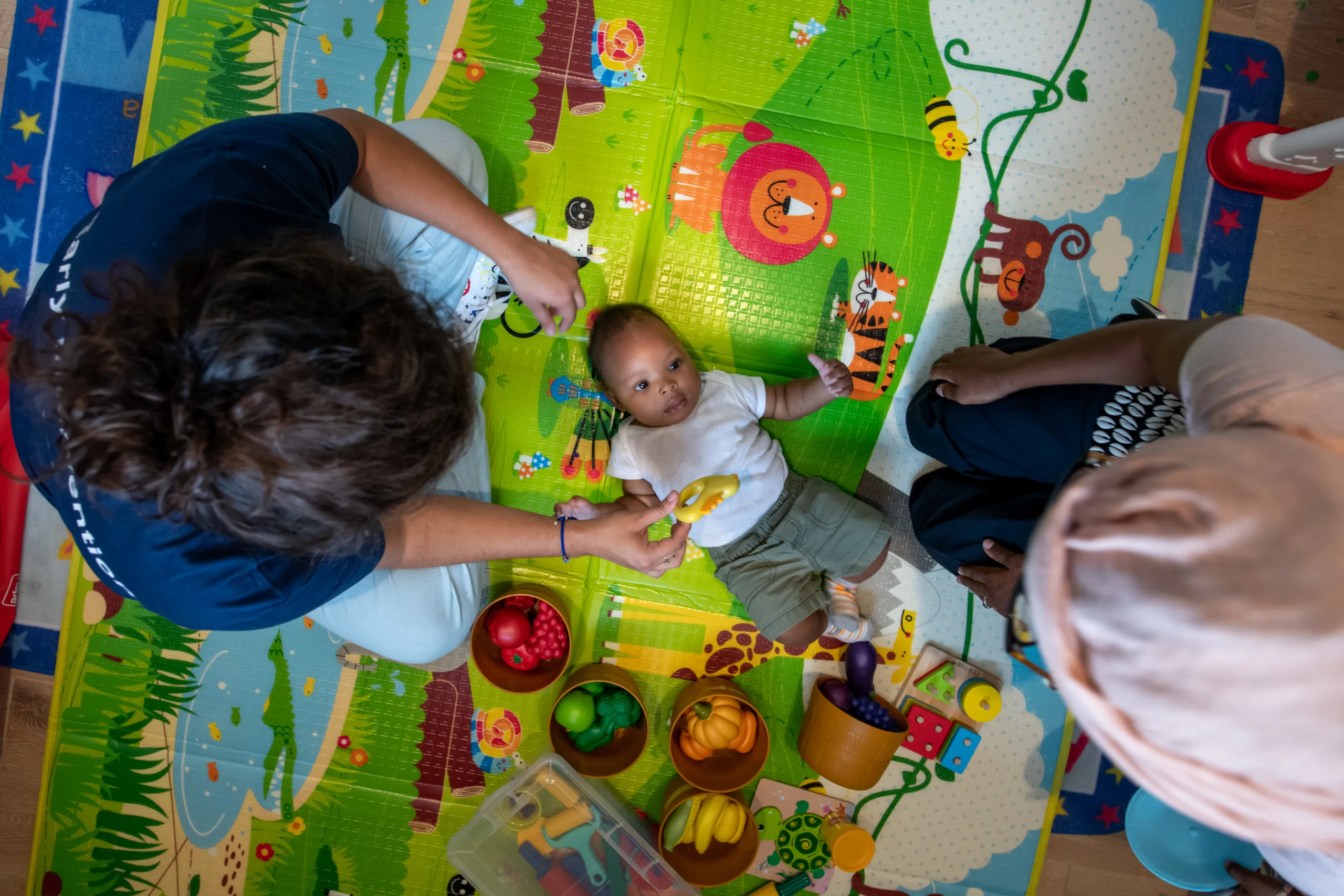 Two caregivers engaging and playing with an infant on a play mat with sensory toys.