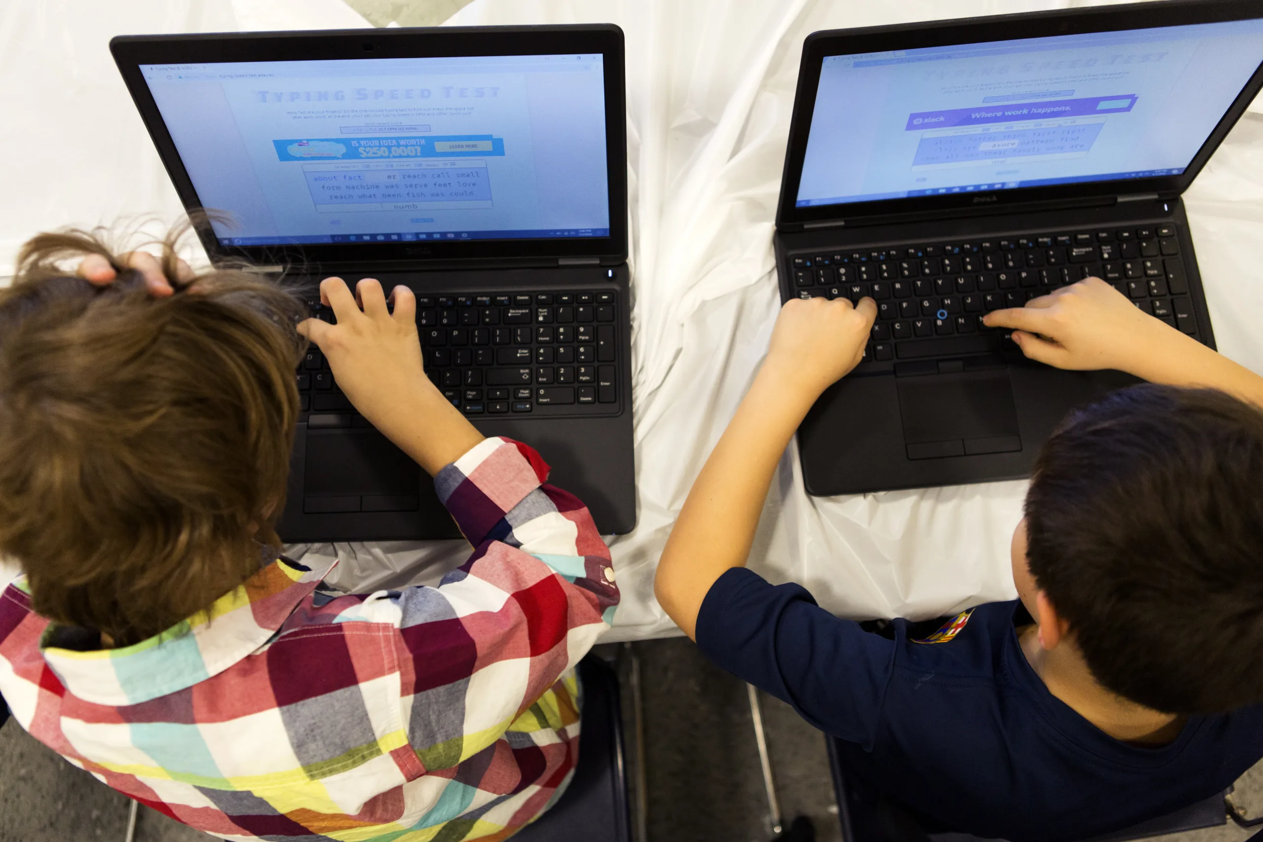 An overhead shot of two children typing on laptops.