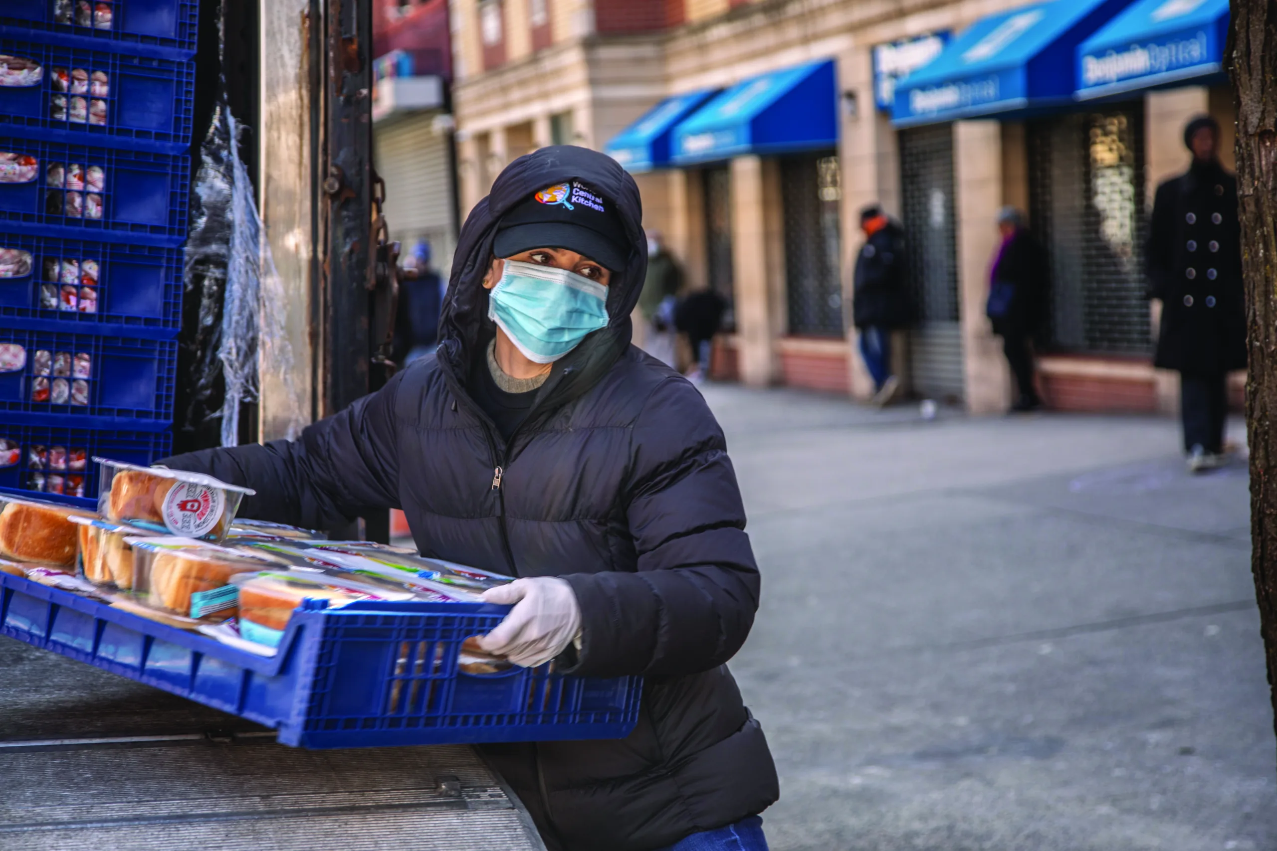 A woman wearing a mask carrying a pallet of food donations lifted from the back of a truck.