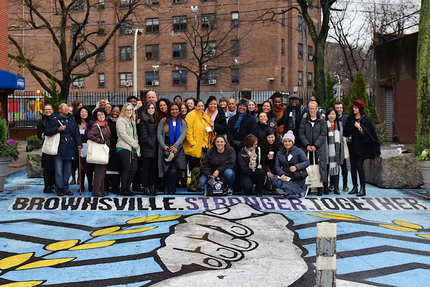 A large group of people posing for a photo in front of a painted mural on a sidewalk reading 