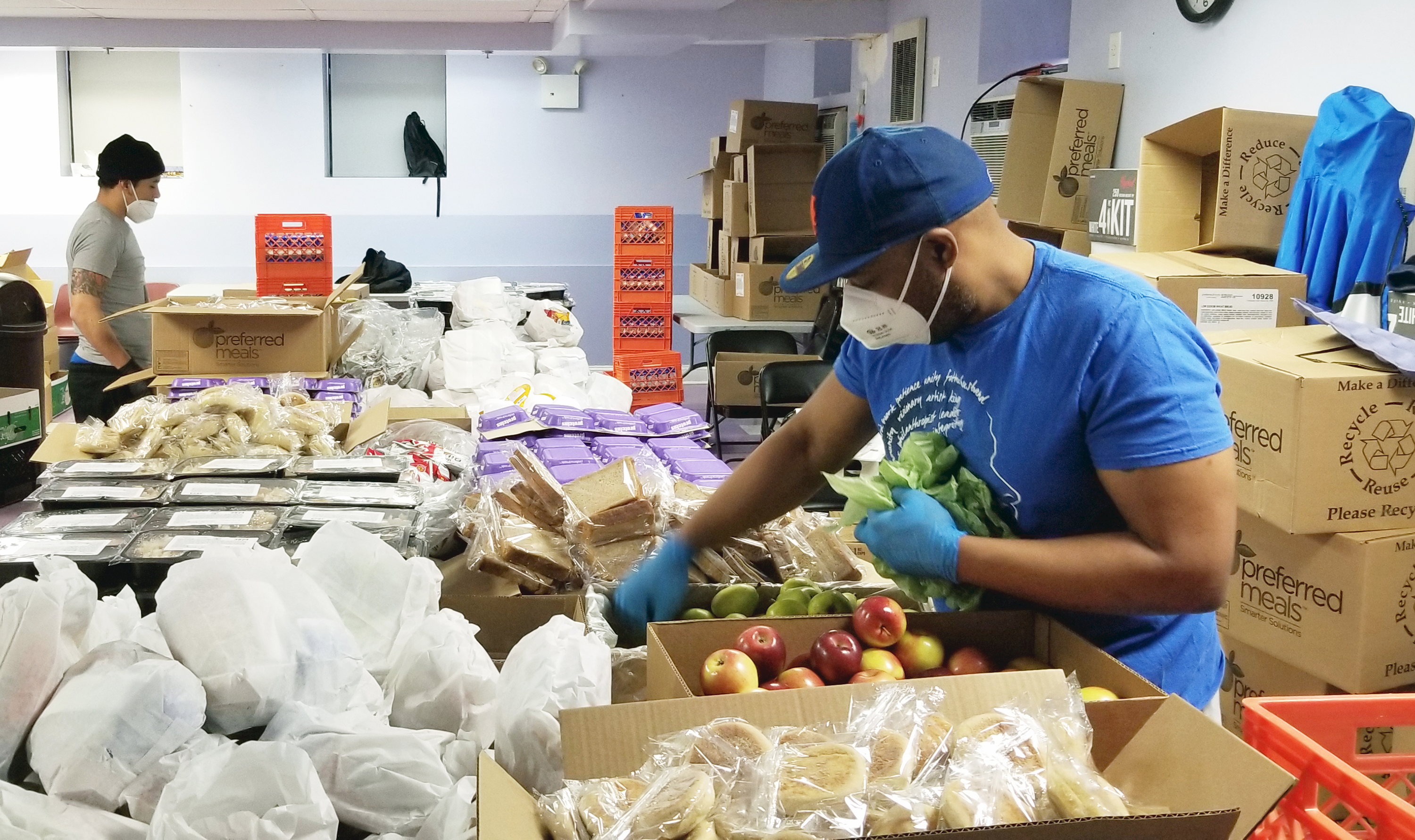 A man wearing a mask working to package emergency food grocery packages in a warehouse setting.