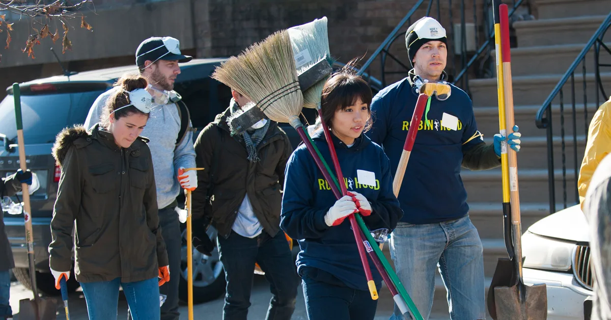 A group of five volunteers wearing Robin Hood shirts and holding brooms and cleaning supplies