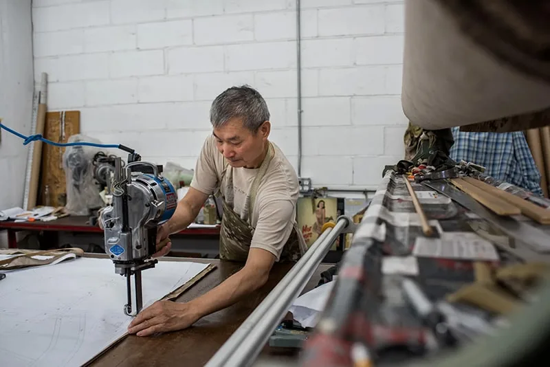An older man of Asian descent using power tools and machinery in a workshop setting.